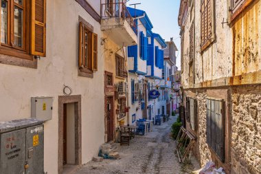 Renkli panjurları ve güneş ışığıyla aydınlanan kaldırım taşı yolu olan eski kasabada büyüleyici dar bir sokak. 3 Ağustos 2025, Ayvalik, Türkiye.