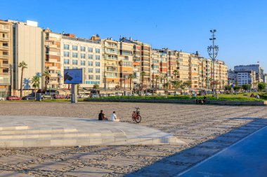 Modern binalarla güneşli şehir meydanı ve sahil şehrindeki insanları rahatlatıyor. 4 Ağustos 2025 İzmir Türkiye.