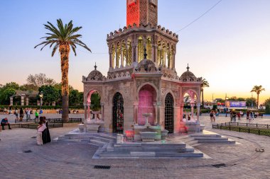 Günbatımında tarihi saat kulesi, aydınlatılmış çeşme ve toplanan insanlar. 4 Ağustos 2025, İzmir Türkiye.