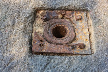 Beton yüzeyinde merkezi delik olan paslı metal plaka..