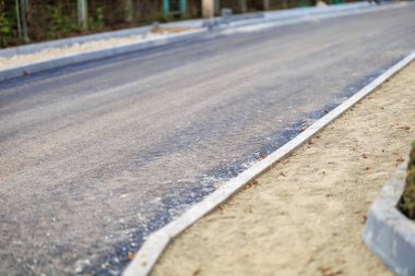Taze asfalt ve çakıllı omuzlu yeni asfalt yol şehir ortamında.