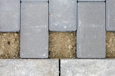 Gri beton kaldırım tuğlalarının yakın planında açıkta kalan toprak desenleri var..