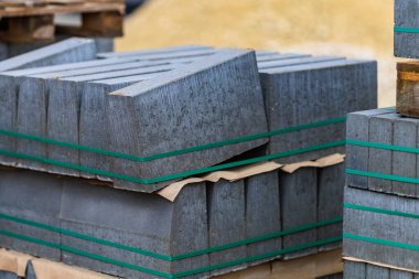 Beton kaldırımlar bir inşaat sahasında düzgün sıralara dizilmiştir. Güneş güçlü blokların üzerinde parlıyor, dokulu yüzeylerini ve yeşil bağlayıcı kayışlarını sergiliyor. Sahne organize çabaları iletir.