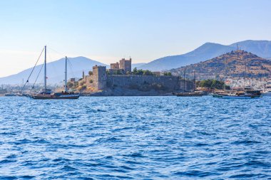 Ege Denizi 'ndeki Bodrum kalesi ve yelkenlileri dağ zeminine karşı. 6 Ağustos 2025, Bodrum Türkiye.