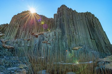 Mavi gökyüzü ve doğal bitki örtüsüne sahip güneş ışığı bazalt sütun oluşumları.