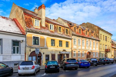 Engelli işareti olan bir binanın önüne park edilmiş arabalı bir sıra bina. Sokak boş ve gökyüzü bulutlu. 14 Aralık 2024 Brasov Romanya