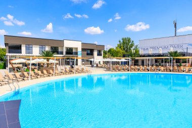 Bir sürü şezlonglu sandalye ve şemsiyeli büyük bir havuz. Havuz bir sürü ağaç ve binalarla çevrilidir. 8 Haziran 2024 Balti Moldova