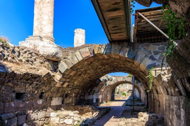 Mavi gökyüzünün altında taş kemer ve sütunları olan antik Roma harabeleri. İzmir, İzmir 'de antik İzmir kalıntıları.