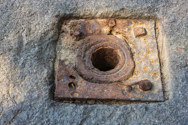 Merkezi delik ve cıvatalarla beton yüzeyde paslı metal plaka.