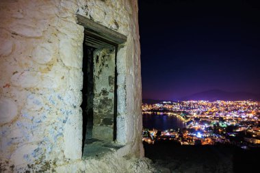 Eski taş yel değirmeninin gece manzarası aydınlatılmış sahil şehri manzarası.