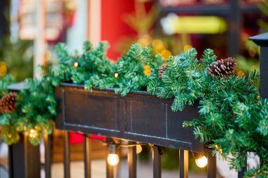 Şenlikli yeşillik ve çam kozalakları sıcak tatil ışıklarıyla süslü korkuluklarda..