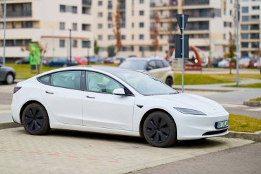 Modern binaların olduğu kentsel alana park edilmiş beyaz elektrikli araba. 12 Aralık 2025 Romanya.