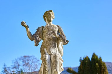 Antik çağlarda, mavi gökyüzüne ve ağaçlara karşı yıpranmış taş heykel. 13 Aralık 2025 Sinaia Romanya.