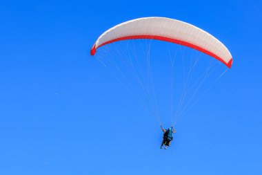Paragliding adventure: duo soaring across clear blue sky.