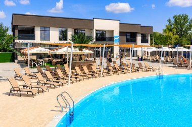 Bir sürü şezlonga ve şemsiyeye sahip bir havuz. Havuz kumlu bir plajla çevrilidir. 8 Haziran 2024 Balti Moldova