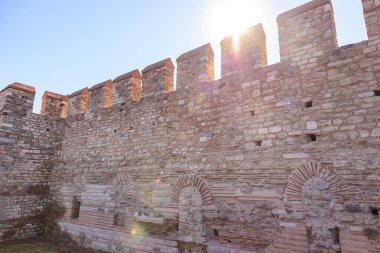 Tarihsel ortamda güneş ışığıyla kaplı antik kale duvarı.