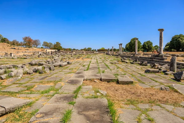 Arka planda birkaç ağaç olan taştan bir geçit. Gökyüzü mavi ve çimenler yeşil. Yunanistan 'ın antik Filippi kentinin kalıntıları