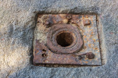 Merkezi delikli beton yüzeye gömülü paslı metal levha..