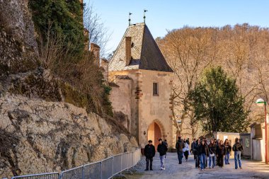 Turistler manzaranın tarihi taş kale girişini keşfediyorlar. 19 Mart 2025, Karlstejn, Çek Cumhuriyeti.