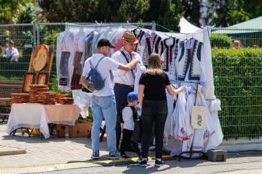 Beyaz yetişkinler ve çocuklar işlemeli kıyafetlerle geleneksel pazarı keşfediyorlar. 22 Mayıs 2025 Balti Moldova.