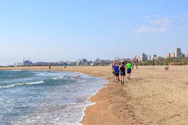 Şehir manzarası olan kumlu bir plajda koşan bir grup insan. 4 Mayıs 2025 Romanya.