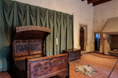 Ortaçağ yatak odası, tarihi kale ortamında süslü ahşap yatak ve duvar halıları. 19 Mart 2025, Karlstejn, Çek Cumhuriyeti.