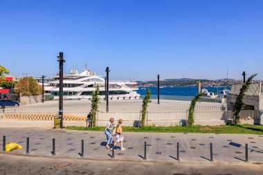 İki olgun kadın açık mavi gökyüzünün altında deniz kenarı boyunca yürüyorlar. 12 Ağustos 2025 İstanbul Türkiye.