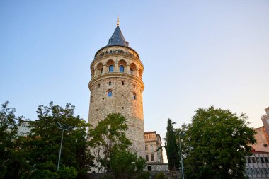 İstanbul 'daki tarihi Galata Kulesi gün batımında ağaçlarla çevrili.