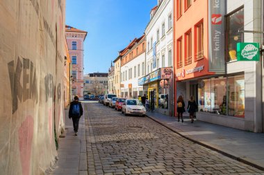Güneşli bir günde renkli binaların yanında yürüyen insanlarla dolu bir cadde. 21 Mart 2025, Ceske Budejovice, Çek.