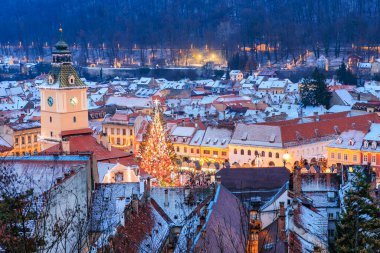 Geceleri ortasında büyük bir saat kulesi olan bir şehir. Şehir Noel ışıklarıyla aydınlanıyor ve merkezinde büyük bir Noel ağacı var.