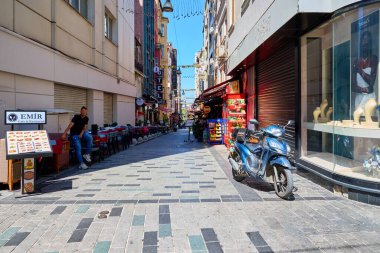 Parlak bir arka sokak, açık bir kafe ve güneşli bir günde park etmiş scooter. 11 Ağustos 2025, İstanbul Türkiye.