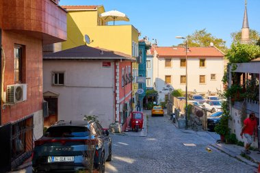 Parke yolu üzerinde binaları ve park edilmiş arabaları olan güneşli Avrupa kentsel caddesi. 11 Ağustos 2025, İstanbul Türkiye.