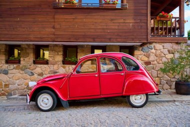 Kırsal ahşap ve taş evin yanına park edilmiş klasik kırmızı klasik bir araba. 14 Ağustos 2025, Sozopol Bulgaristan.