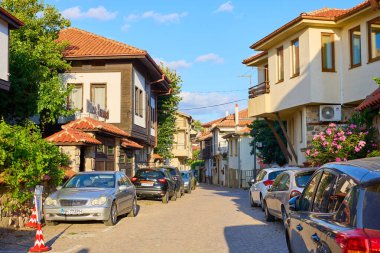 Geleneksel Avrupa köyünün sessiz, güneşli caddesinde evler arasında arabalar var. 14 Ağustos 2025, Sozopol Bulgaristan.
