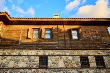 Mavi gökyüzü ve bulutların altında taş temeli olan tarihi ahşap bir ev..