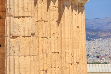 Duvar taştan yapılmış ve pürüzlü bir dokusu var. Aşağıdaki şehrin manzarası nefes kesici, Atina akropolünde sütunlar