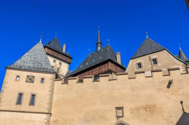 Ortaçağ kale duvarı ve açık mavi gökyüzüne karşı kule. 19 Mart 2025, Karlstejn, Çek Cumhuriyeti.