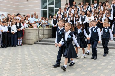 Okul seremonisinde, beyaz üniformalı genç öğrencilerle birlikte yürüyoruz. 2 Eylül 2024 Balti Moldova.