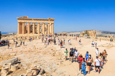 Büyük bir grup insan büyük bir binanın etrafında toplanıyor, muhtemelen bir tapınak ya da anıt. Gökyüzü açık ve mavidir, ve güneş parlıyor. 9 Ağustos 2024 Atina Yunanistan