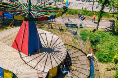 Salıncaklı renkli bir atlıkarınca ve güneşli parkta dinlenen insanlar. 22 Mayıs 2025 Balti Moldova.