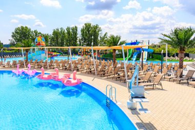 Pembe ve mavi şamandıralı bir havuz ve bir sürü şezlong. Havuz ağaçlar ve palmiye ağaçlarıyla çevrilidir. 8 Haziran 2024 Balti Moldova