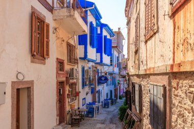 Akdeniz köyünde renkli binalar ve mavi aksanlarla büyüleyici dar bir cadde. 3 Ağustos 2025, Ayvalik, Türkiye.