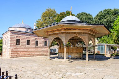 Tarihi minder mimarisi: ağaçlarla çevrili kubbeleri olan çeşme ve bina. 12 Ağustos 2025 İstanbul Türkiye.