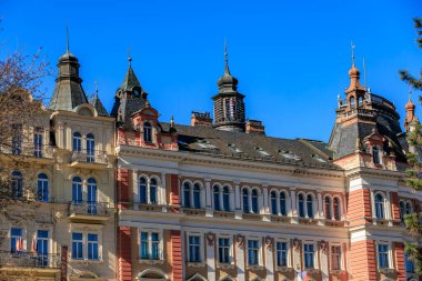 Mavi gökyüzünün altında süslü cepheleri ve kuleleri olan tarihi Avrupa mimarisi. 19 Mart 2025, Karlovy Vary, Çek Cumhuriyeti.