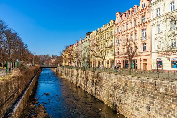 Güneşli bir günde Karlovy nehri boyunca uzanan renkli tarihi binalar değişir. 18 Mart 2025, Karlovy Vary, Çek Cumhuriyeti.