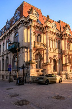 Şık tarihi bina ve şehir merkezinde günbatımında modern araba. 3 Mayıs 2025 Romanya.