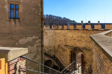 Ortaçağ kale avlusunda taş duvarlar ve güneş ışığında kemerli kapılar..