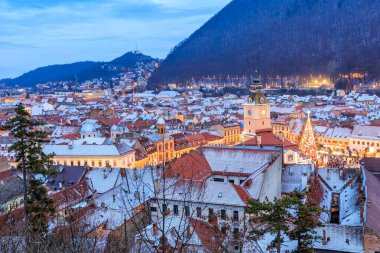 Geceleri ortasında Noel ağacı olan bir şehir. Şehir karla kaplı ve ışıklar açık.