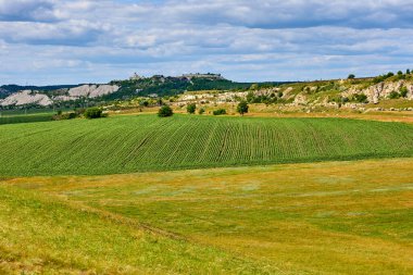 Yeşil tarlaları ve bulutlu gökyüzünün altındaki uzak tepeleri olan yuvarlanan tepeler..