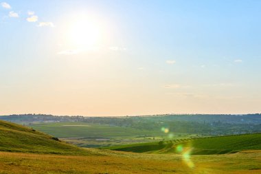 Güneşli bir manzara. Yuvarlanan tepeler ve berrak gökyüzünün altındaki uzak bir köy..